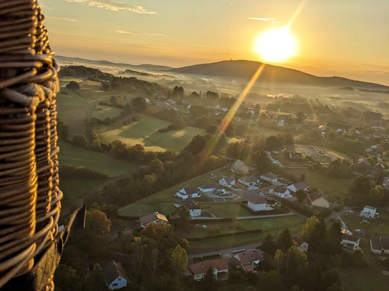 Paysage brumeux au lever du soleil avec des maisons dispersées et des arbres, vu depuis le panier d'une montgolfière