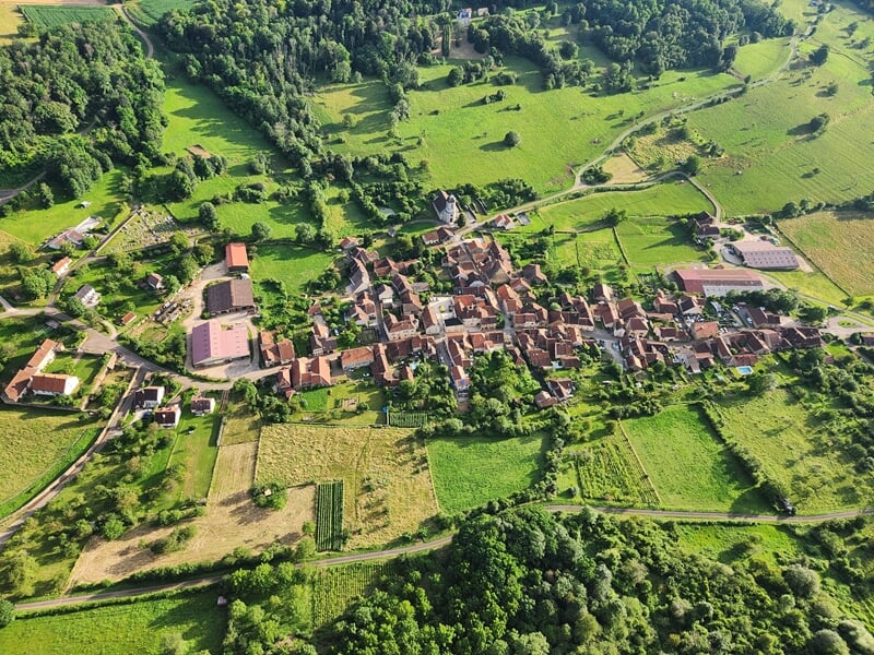 Vue aérienne d'un village rural entouré de prairies verdoyantes et de collines boisées
