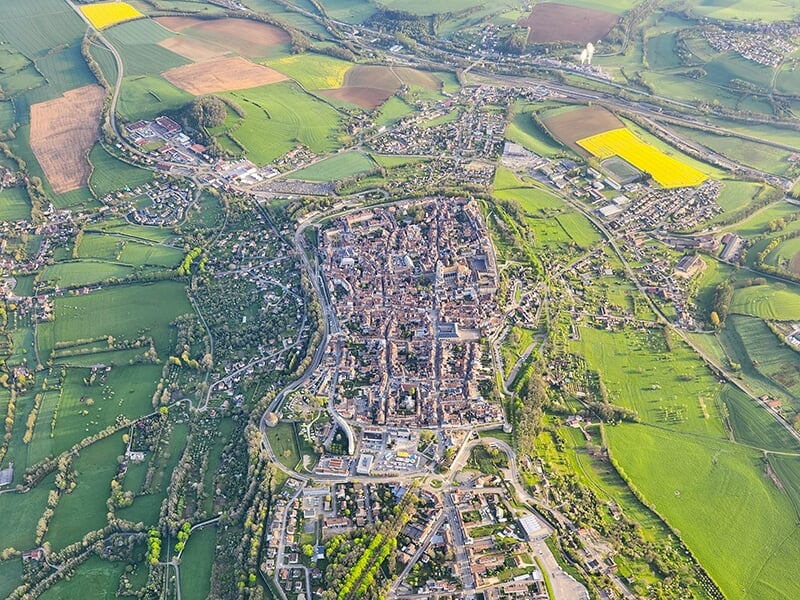 Vue aérienne d'une ville médiévale entourée de champs verdoyants et de collines.