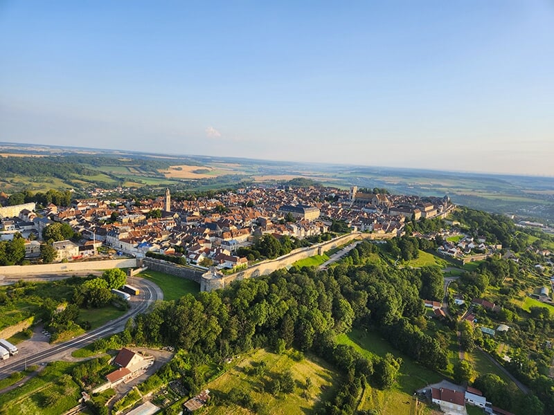 Panorama d'une ville fortifiée avec des remparts dominant une campagne vallonnée.