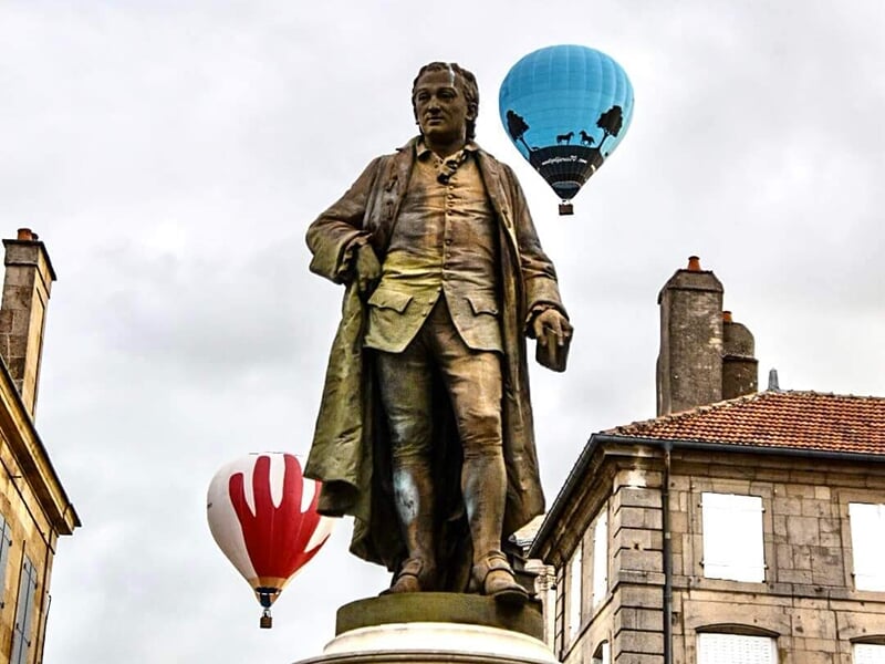 Statue d'un personnage historique, avec des montgolfières flottant dans le ciel en arrière-plan.