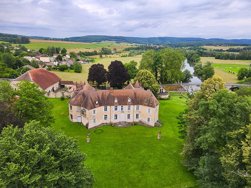 Château élégant entouré d'un parc verdoyant, avec une rivière et des villages en arrière-plan.
