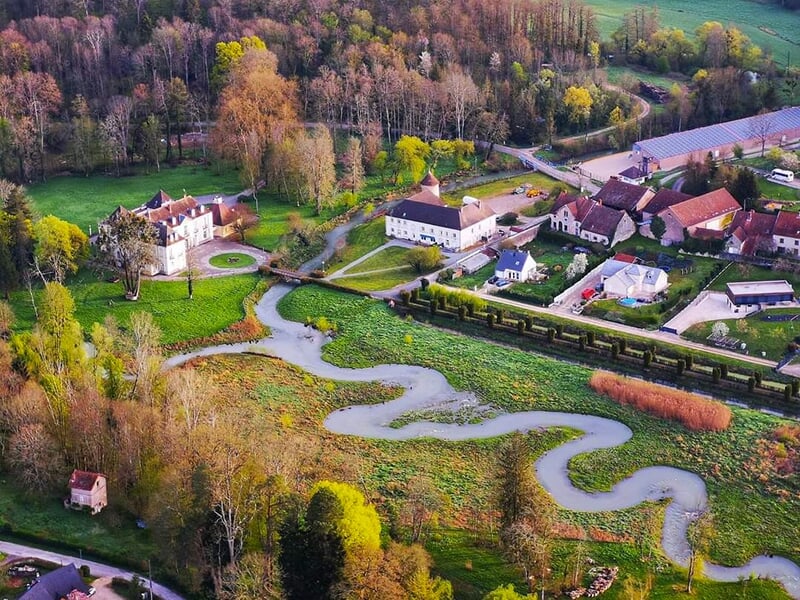 Domaine champêtre avec une rivière sinueuse, des bâtiments historiques et une végétation luxuriante.