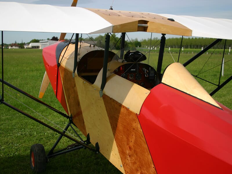 Gros plan sur le cockpit d’un biplan en bois et toile avec une peinture rouge et naturelle, tableau de bord équipé d’instruments de vol, siège en bois et verrière ouverte, stationné sur un terrain ver