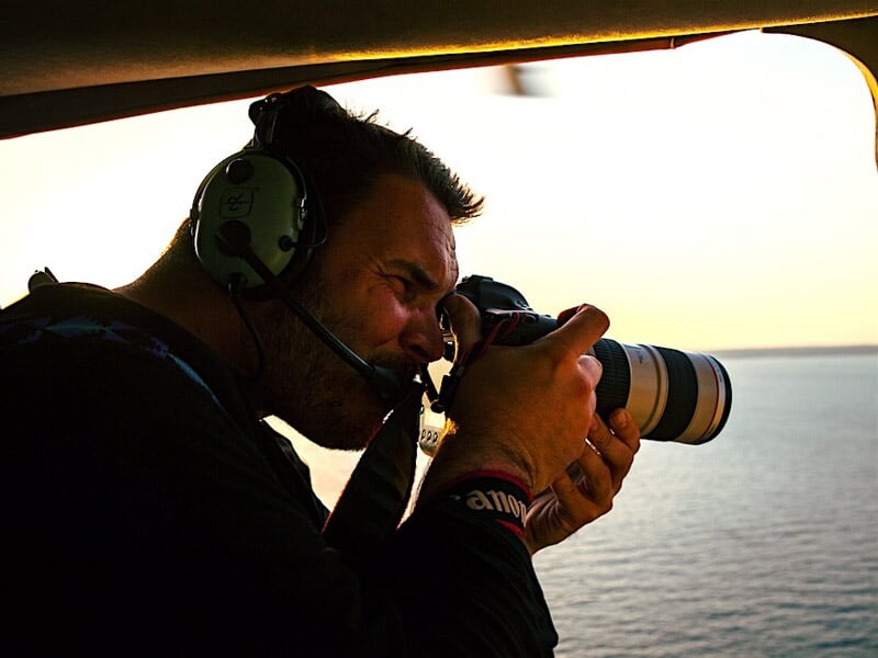 Homme avec casque audio et micro prenant une photo avec un appareil photo à objectif téléobjectif depuis un hélicoptère.