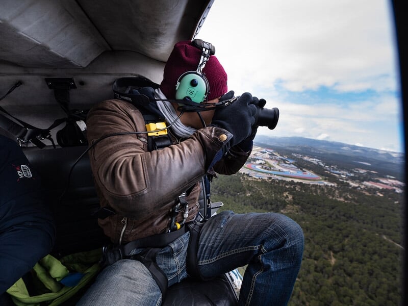 Passager en tenue d'hiver avec casque et lunettes prenant une photo à travers la porte ouverte d'un hélicoptère en vol.