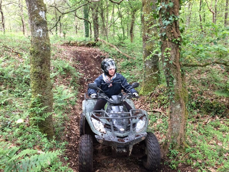Personne en tenue de protection conduisant un quad sur un sentier forestier étroit entouré d'arbres verts.