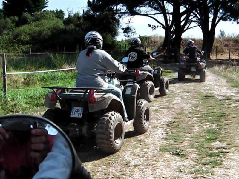 Convoi de quads sur un chemin de terre entouré de végétation, avec un ciel bleu clair en arrière-plan.