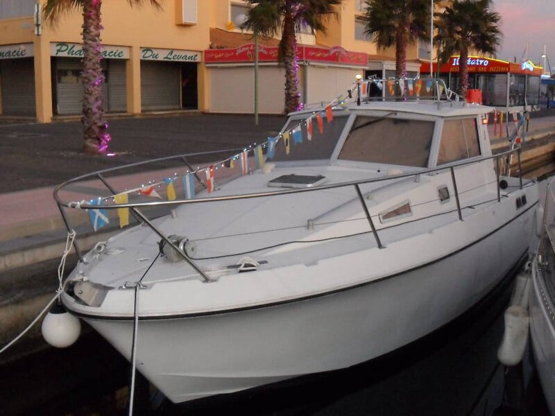 Bateau blanc amarré au quai avec des décorations colorées, devant des commerces et des palmiers au coucher du soleil.