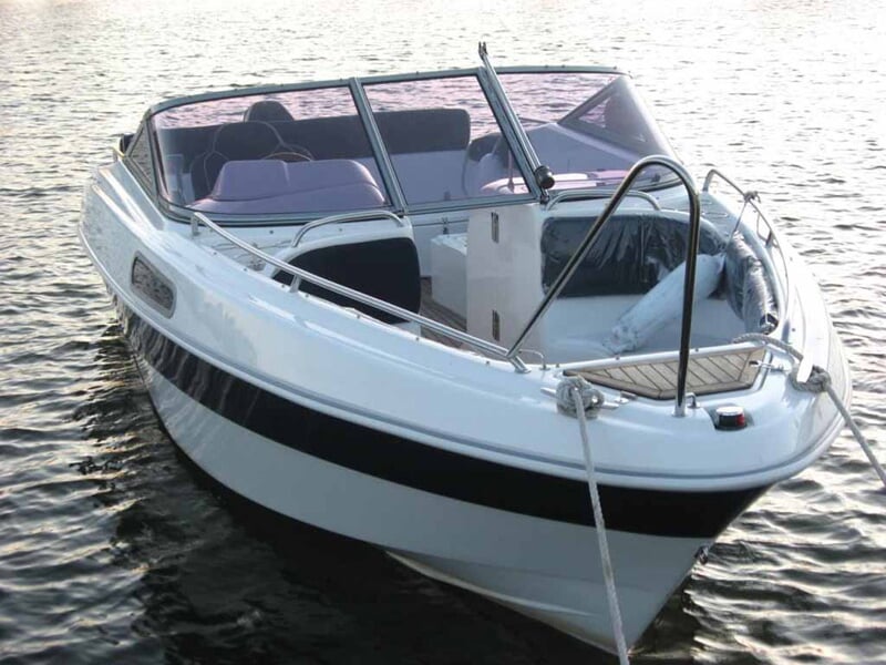 Petit bateau de plaisance blanc avec une bande noire, flottant sur l'eau calme au bord d'un quai.