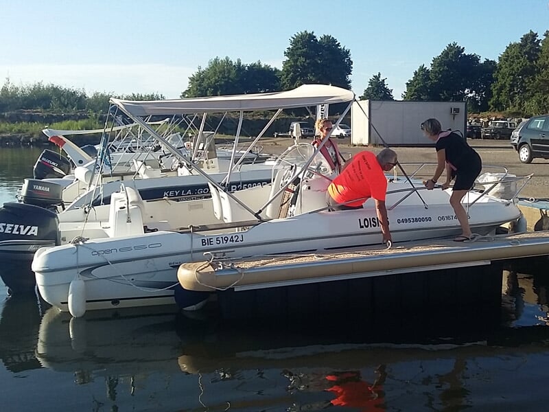 Personnes montant sur un bateau blanc amarré dans un port sous un ciel dégagé.