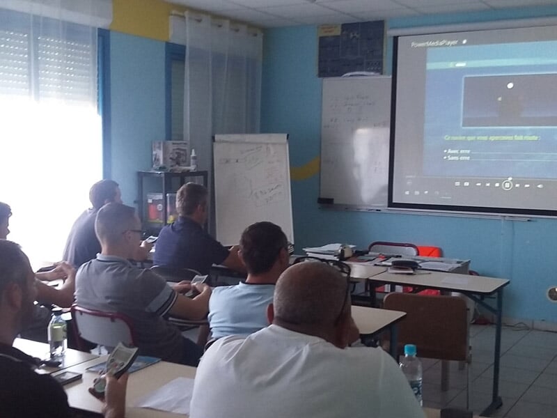 Groupe d'adultes assis en classe regardant un écran lors d'une formation en salle.