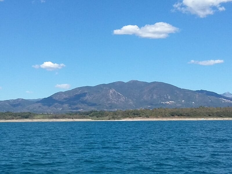 Vue sur une montagne depuis la mer avec un ciel bleu et quelques nuages blancs.