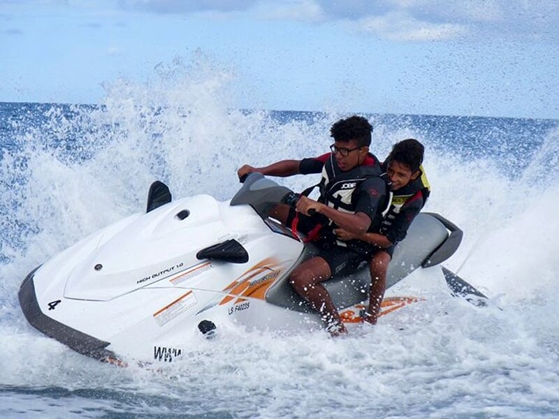 Deux personnes sur un jet-ski blanc, naviguant à grande vitesse sur une mer agitée, avec des éclaboussures d’eau autour d’eux.