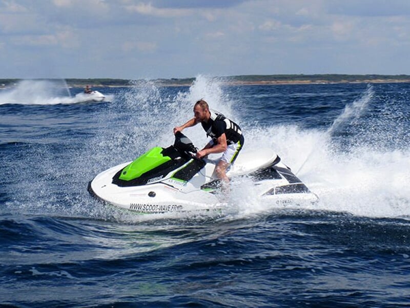 Un homme seul pilotant un jet-ski vert et blanc, fonçant sur les vagues avec un effet de vitesse et d’adrénaline.