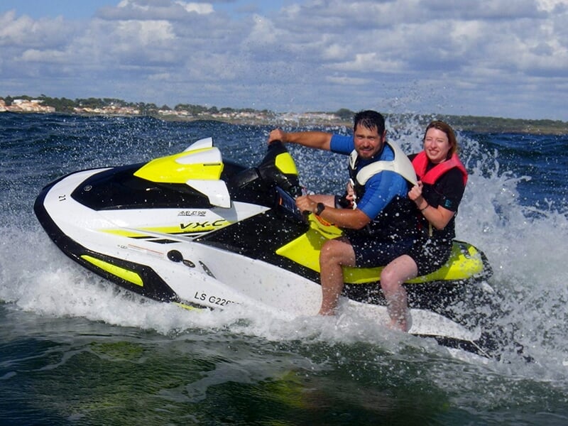 Un homme et une femme sur un jet-ski jaune et noir, profitant ensemble d’une balade en mer avec le sourire.