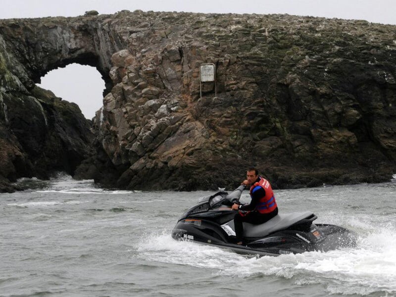 Pilote sur un jet-ski noir, explorant une zone rocheuse avec une arche naturelle en arrière-plan