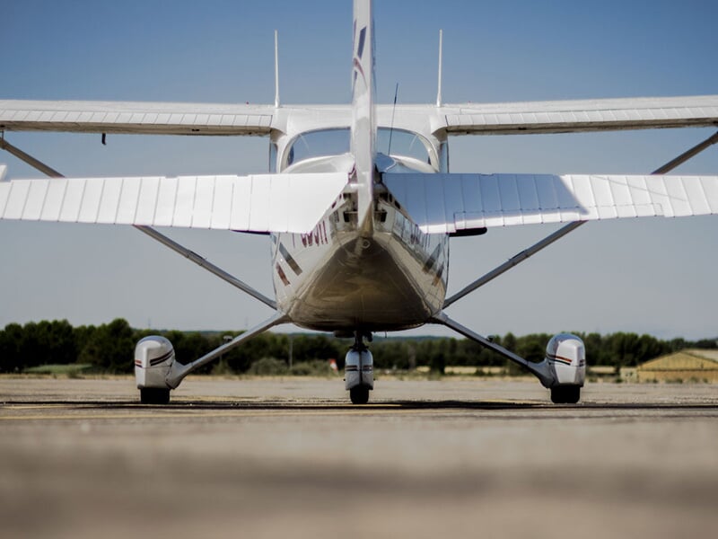Vue frontale d'un petit avion blanc posé sur la piste, avec ses ailes étendues et un ciel clair.