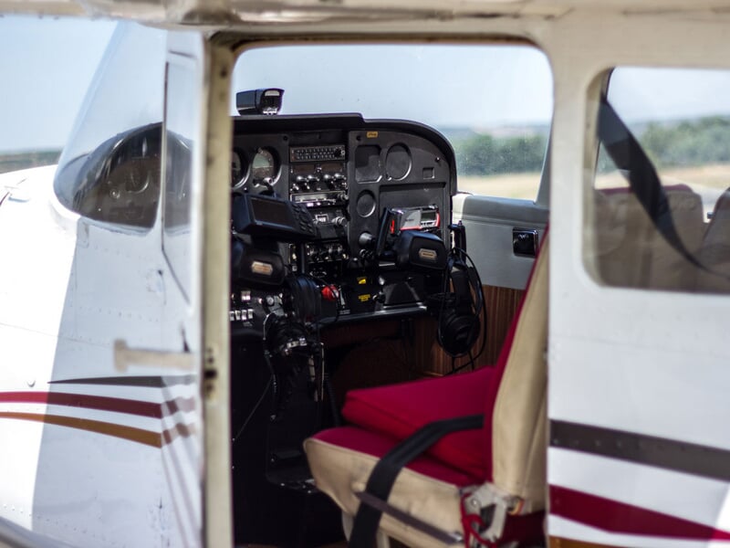 Intérieur d'un petit avion montrant le poste de pilotage avec siège beige et tableau de bord rempli d'instruments.