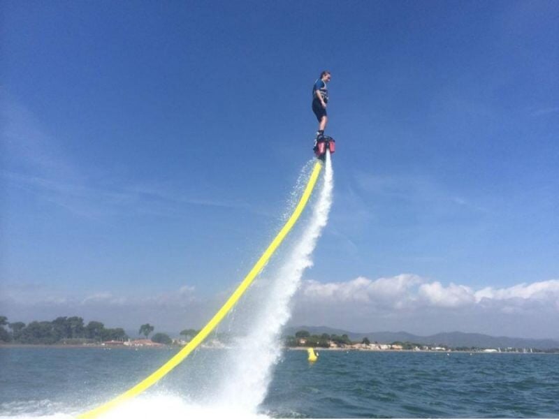 une personne vole en flyboard au-dessus de l'eau avec la côte méditerranéenne en arrière plan