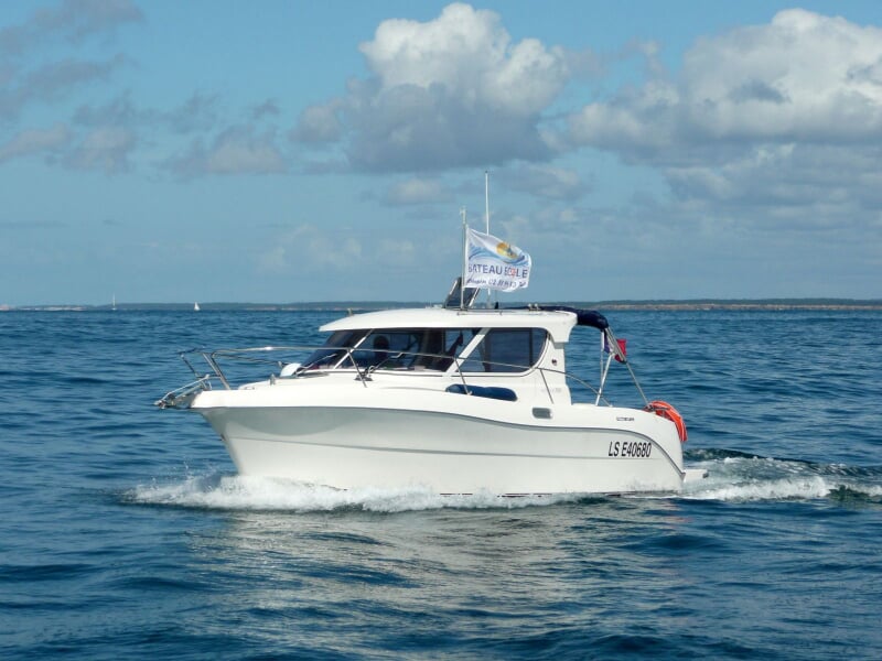 Bateau blanc à moteur naviguant sur une mer calme sous un ciel bleu avec quelques nuages blancs.