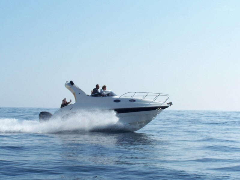 Bateau rapide blanc avec plusieurs personnes à bord, avançant sur une mer calme sous un ciel clair.