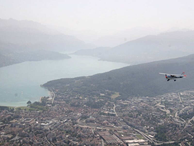 Avion léger volant au-dessus d'une ville au bord d'un grand lac entouré de montagnes dans la brume.