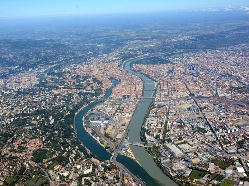 Vue aérienne de la ville de Lyon avec la rivière Rhône traversant le paysage urbain sous un ciel clair.