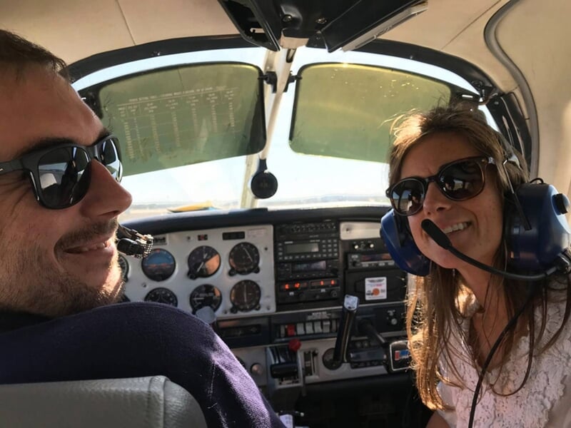 Deux personnes souriantes portant des casques avec micro à l'intérieur du cockpit d'un petit avion léger.
