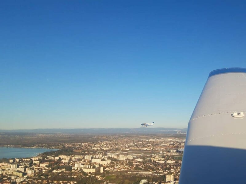 Vue depuis un avion en vol montrant un autre petit avion volant au-dessus d'une ville sous un ciel dégagé.