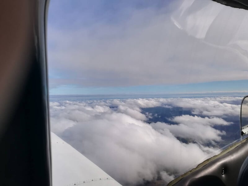 Vue depuis l'intérieur d'un avion montrant un ciel nuageux avec un épais tapis de nuages blancs en dessous.