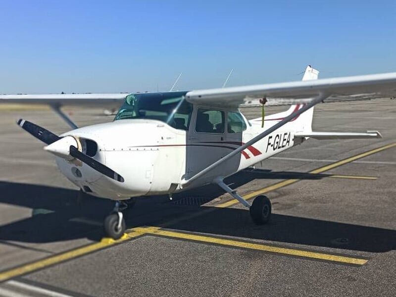 Petit avion blanc immatriculé F-GLEA stationné sur une piste d'aéroport sous un ciel bleu clair et ensoleillé.