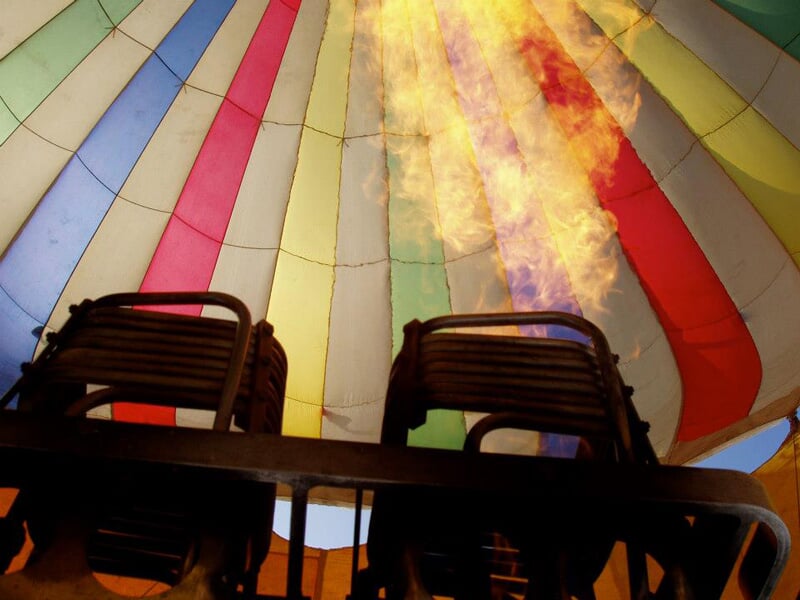Intérieur d’une montgolfière montrant le brûleur en action, avec des flammes vives éclairant la toile multicolore tendue au-dessus.