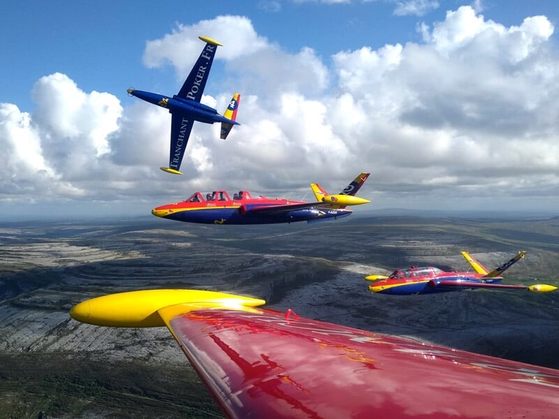 des avions de chasse rouges, jaunes et bleus volent en formation au-dessus des paysages plats de la région parisienne