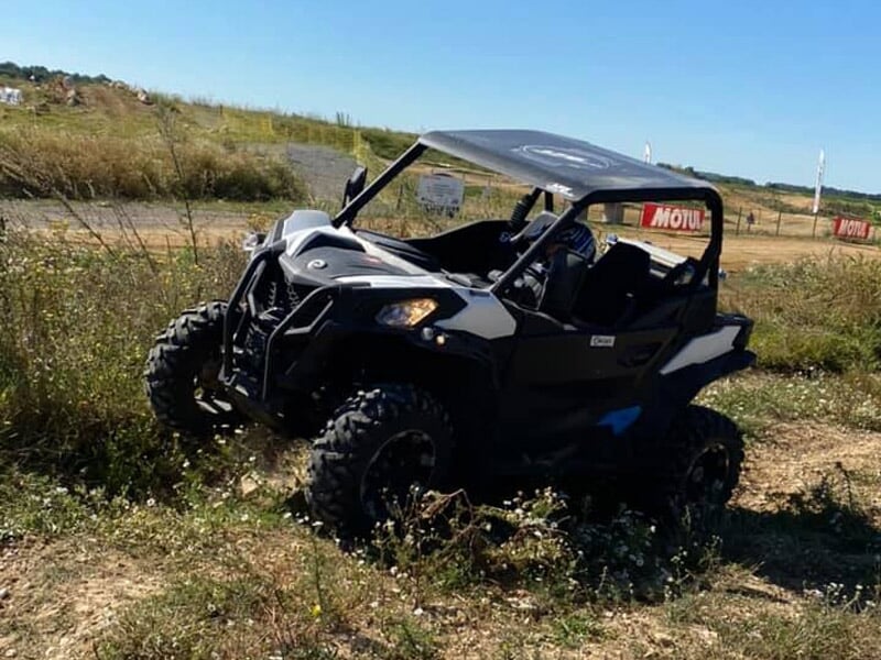 Buggy noir à l’arrêt sur un chemin de terre bordé d’herbes sauvages, sous un ciel bleu clair.