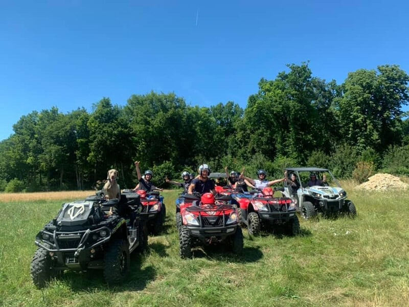 Groupe de personnes posant sur des quads et un buggy, en bordure de forêt, sous un ciel bleu dégagé, en pleine nature.