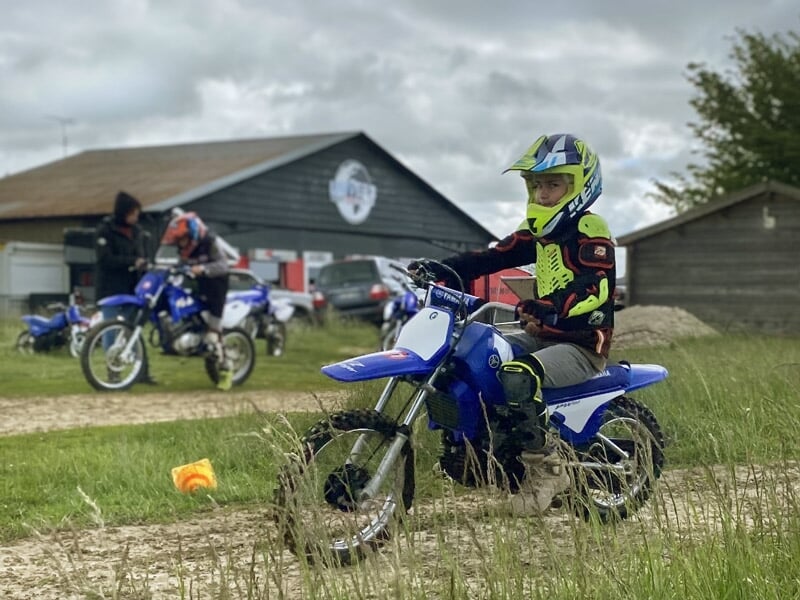 Jeune enfant en tenue de protection sur une moto bleue lors d'un stage de pilotage moto en extérieur.