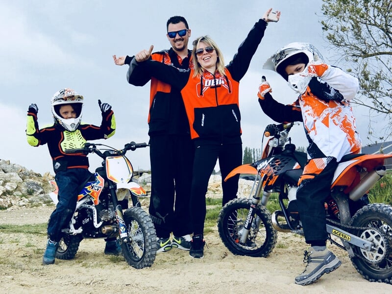 Groupe de trois personnes souriantes avec leurs motos tout-terrain sur un terrain de motocross.