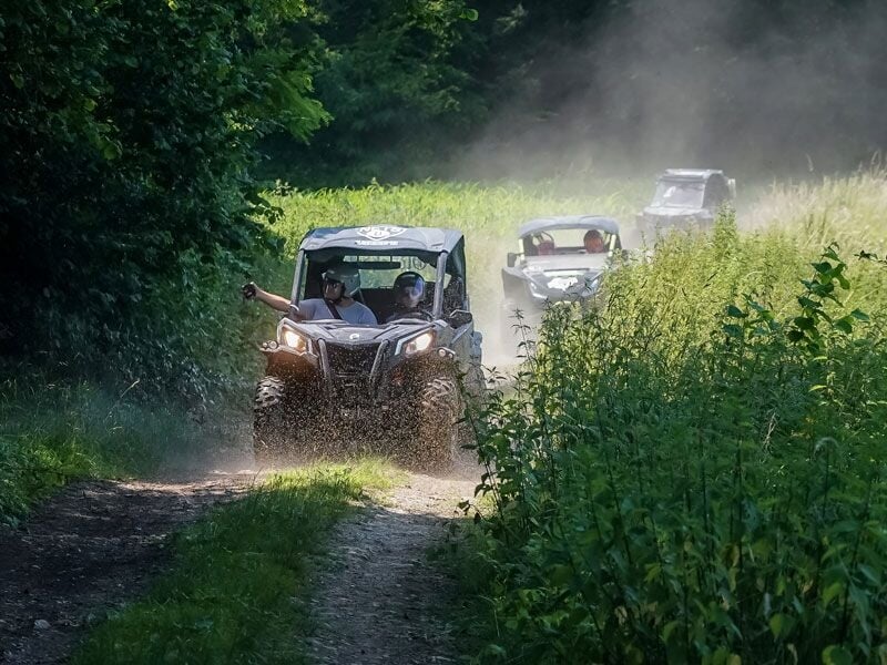 Trois quads avancent sur un chemin de terre entouré de végétation dense et de buissons verts sous un ciel clair.