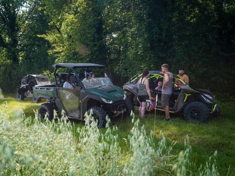 Groupe de personnes discutant près de quads garés dans une clairière entourée d'arbres et de végétation verte.