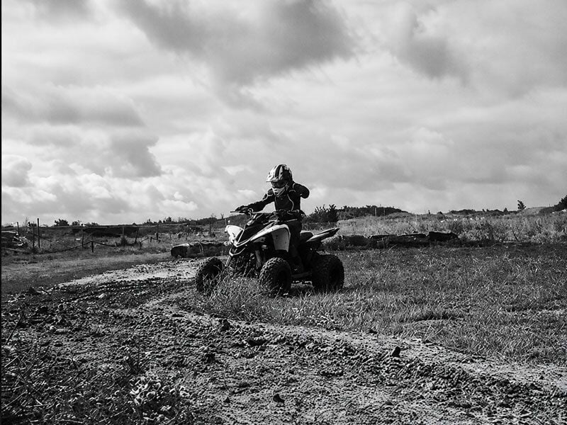Un conducteur de quad traverse un chemin boueux dans un paysage naturel, photo en noir et blanc.