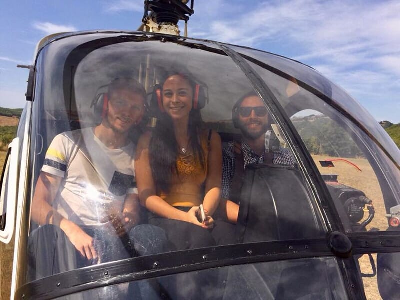 Trois personnes assises dans un hélicoptère, souriant et portant des casques avec micro.