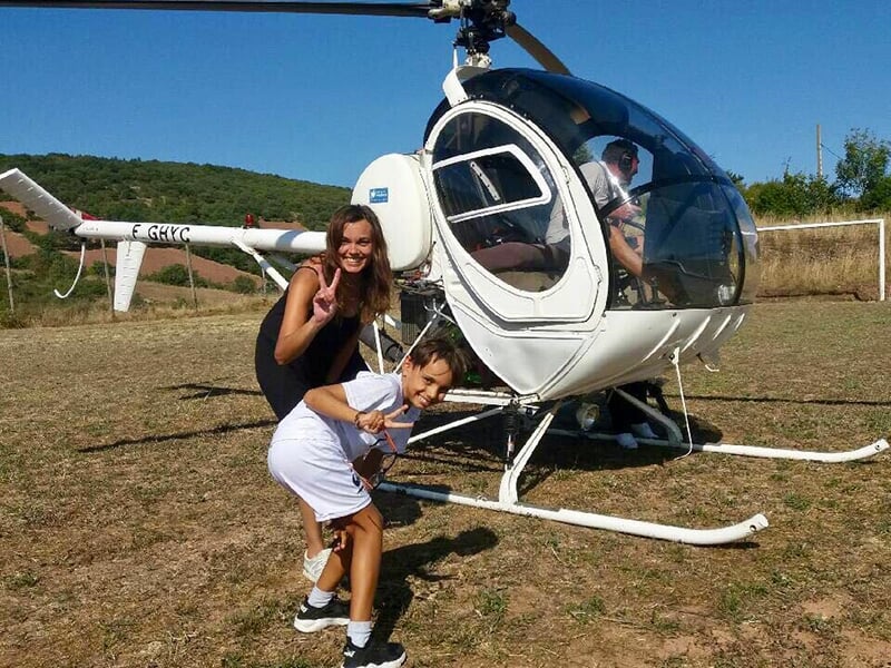 Femme et enfant posant devant un hélicoptère blanc, tous deux souriant et faisant le signe de la paix.