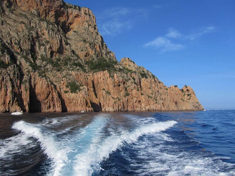 Vue depuis un bateau montrant une côte rocheuse escarpée avec des montagnes en arrière-plan.
