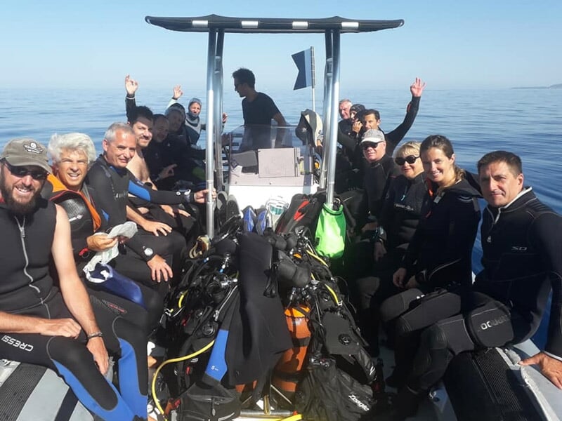 Groupe de plongeurs en combinaison noire assis sur un bateau, prêts pour une plongée.