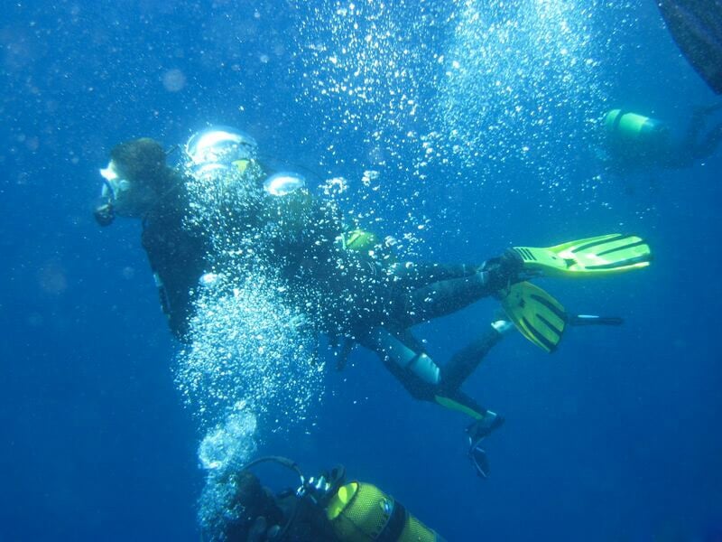 Trois plongeurs sous l'eau, entourés de bulles, explorant un site de plongée en mer.