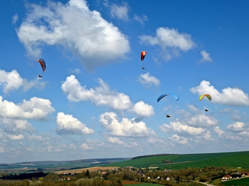 Des parapentes planent dans le ciel bleu au-dessus de la campagne