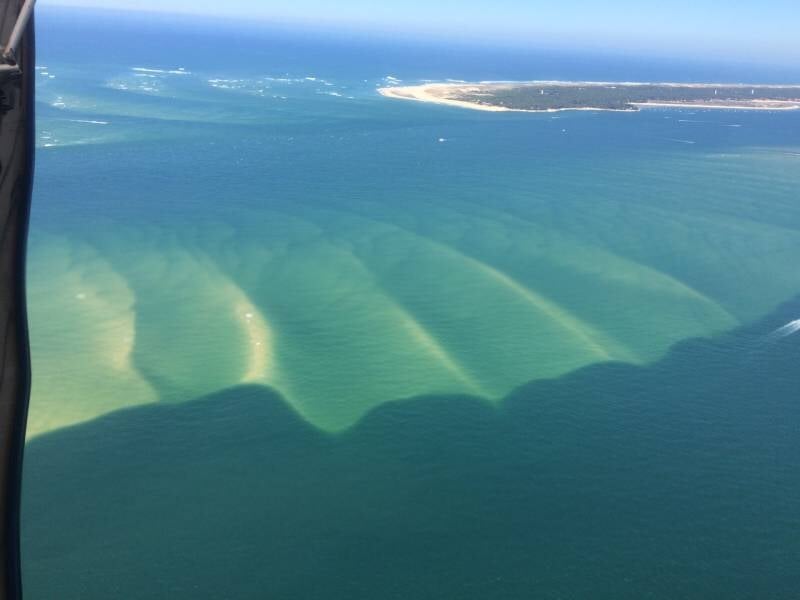 Vue aérienne d'une côte avec des bancs de sable visibles sous l'eau turquoise depuis un avion ultraléger.