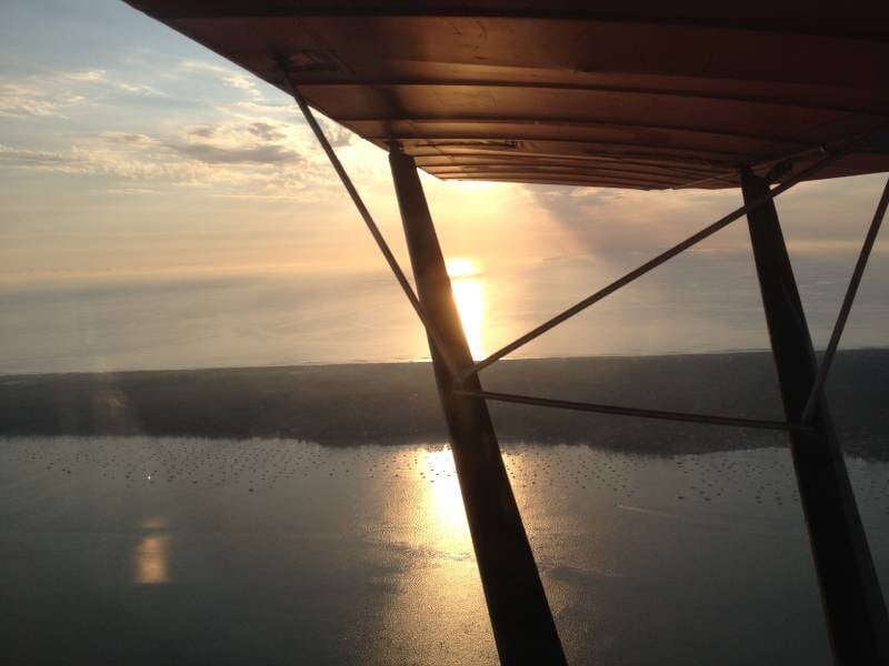 Coucher de soleil vu depuis un avion ultraléger avec la mer calme et une bande de terre à l'horizon.