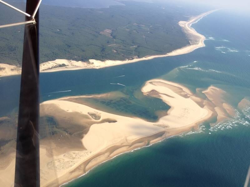Paysage côtier vu depuis le ciel, montrant des plages de sable et des eaux peu profondes lors d'un vol en ULM près du Cap Ferret.